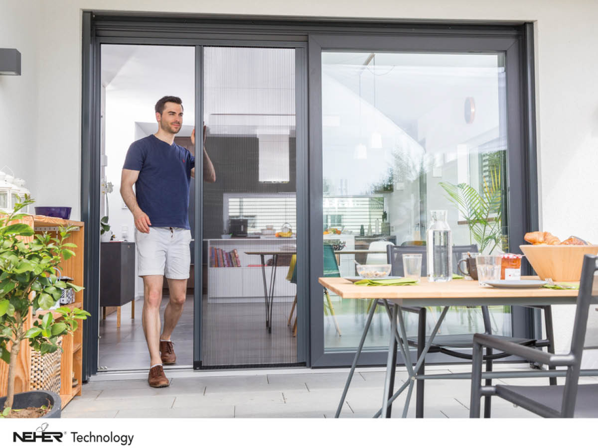 Insektenschutz. Ein Mann steht an einer Plisseetüre, die auf die Terrasse führt.